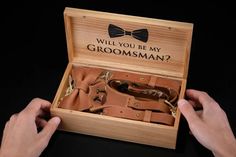 two hands holding an open wooden box with brown leather items in it that says, will you be my groomsman?