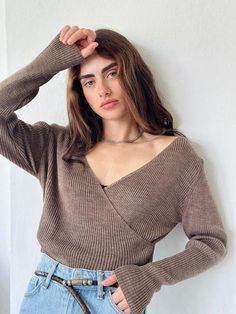 a woman wearing a sweater and jeans poses for the camera with her hands on her head