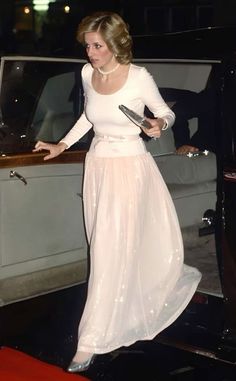 a woman in a long white dress stepping out of a car with her hand on the door handle