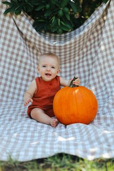 a baby sitting next to a pumpkin on a blanket