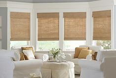 a living room filled with white furniture and lots of windows covered in shades of beige