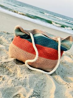 a crocheted bag sitting on top of a sandy beach next to the ocean