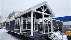 a blue and white tiny house sitting on top of snow covered ground next to a yellow truck