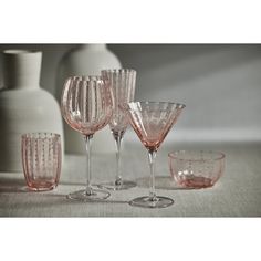 pink wine glasses are lined up on a table next to a vase and other glassware