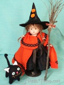 the doll is dressed in an orange dress and black hat with a cat on her lap