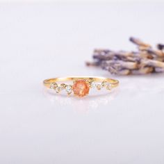 a gold ring with an orange stone surrounded by small white stones and lavender flowers on a white background