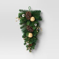 a green christmas tree with pine cones and bells hanging from it's side on a white wall