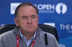 a man sitting in front of a microphone wearing a gray sweater and red lanyard around his neck