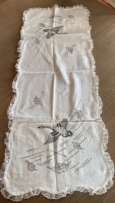 an embroidered table runner with birds on it and lace trim around the edges, sitting on a wooden floor