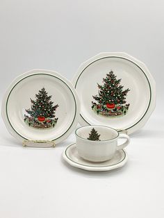 three plates with christmas trees on them are next to a cup and saucer set