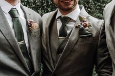 three men in suits and ties standing next to each other with one man wearing a flowered boutonniere