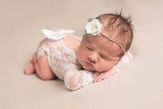 a newborn baby is laying on her side wearing a headband and white flower in it's hair