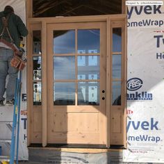 a man standing on a ladder in front of a wooden door with glass panes