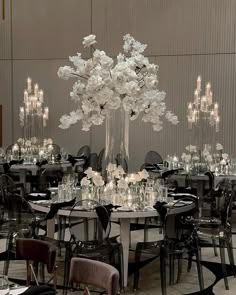 an elegant dining room set up with black chairs and white flowers in tall vases