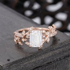 a ring with an emerald stone surrounded by leaves and diamonds on a wooden surface in front of a black background