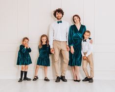 a family posing for a photo in front of a white wall wearing green velvet outfits