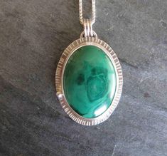 "Here is a handmade pendant made with a lovely malachite and sterling silver. The stone is oval in shape and bright green with a subtle pattern within and a perfect polish.  I set the stone in a fine silver bezel with a sterling silver back plate that I textured around the edge.  I added a little ball of recycled silver at the side.  The pendant measures approx. 1\" by 1 1/2\" (37mm by 27mm) The sterling silver chain is 20\" long with a lobster clasp." Green Oval Malachite Jewelry, Oval Green Malachite Jewelry, Green Sterling Silver Oval Cabochon Jewelry, Green Oval Necklace With Large Stone, Oval Green Necklace With Large Stone, Green Oval Malachite Necklaces, Green Oval Malachite Necklace, Green Oval Large Pendant Jewelry, Lavender Silk