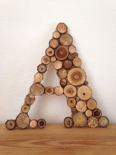 a wooden letter made out of logs on a shelf next to a wall with a white background