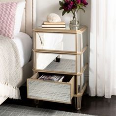 a nightstand with flowers on top of it next to a white bedspread and pillows