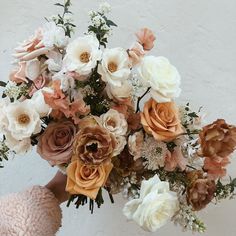 a person holding a bouquet of flowers in their hand with the background painted white and peach