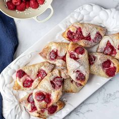 raspberry crescent pastries on a white plate next to a bowl of strawberries