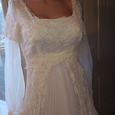 a white wedding dress on display in front of a window with sheer fabric and lace