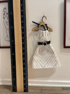 there is a dress hanging on the wall next to a ruler and framed pictures with drawings