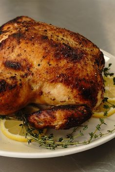 a whole chicken on a plate with lemons and herbs