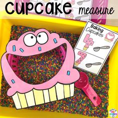 a cupcake measure game in a yellow bin with sprinkles and scissors