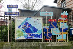 several street signs are displayed in front of a fenced area with trees and bushes