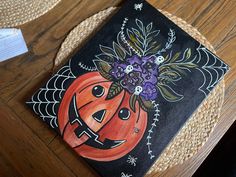 a pumpkin decorated with purple flowers on top of a wooden table next to a card