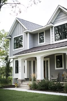 a gray house with white trim on the front and side windows, grass in front