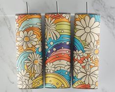 three colorful towels hanging on a towel rack with flowers and circles painted on them in front of a marble wall