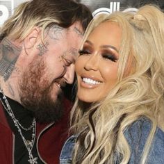 a man and woman hugging each other in front of a red carpeted wall with tattoos on