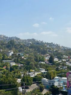 a city with lots of trees and houses on the hill side, in front of a blue sky