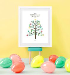 a christmas tree is surrounded by balloons in front of a white frame on a yellow wall