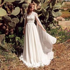 a woman standing in front of a cactus wearing a white wedding dress with sheer sleeves