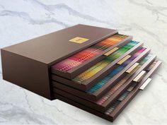 a stack of colored pencils sitting on top of each other in front of a black box