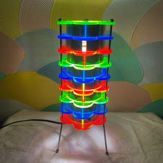 a multicolored lamp sitting on top of a white bed next to a wall