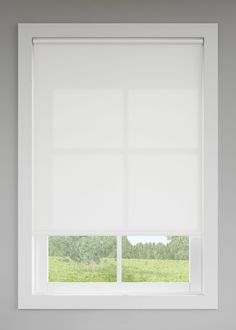 a window with white roller shades in a room that has grass and trees behind it