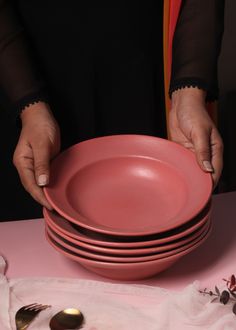 a woman is placing plates on top of each other in front of a pink table cloth