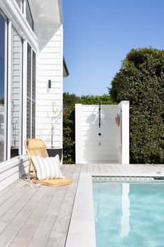 a wooden deck next to a swimming pool with a chair on the side and an open sliding glass door