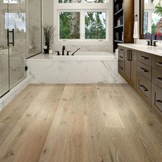 a large bathroom with wood floors and marble tub in the center, along with two sinks