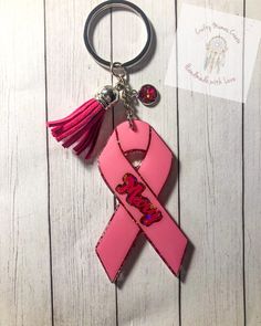 a pink ribbon shaped keychain with a tassel hanging from it's side