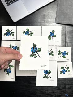 several blue flowers on white cards with green leaves are being held by a person's hand