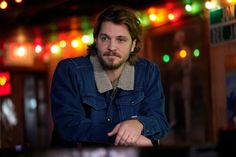 a man sitting at a table with his arms crossed in front of him and colorful lights behind him