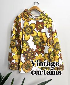 a yellow and brown flowered shirt hanging on a wall next to a plant with the words vintage curtains