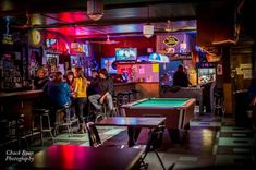 a group of people playing pool in a bar with neon lights on the walls and tables