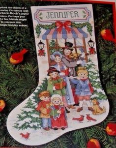 a cross stitch christmas stocking hanging from a tree with red berries around it and two children