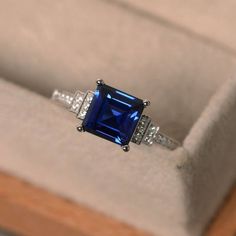 an engagement ring with a blue stone surrounded by white diamonds in a velvet box on display